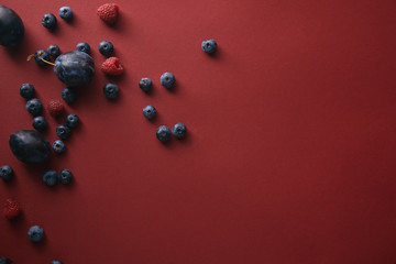 top view of blueberries, raspberries and plums on red surface