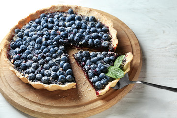 Wooden board with delicious blueberry pie on table