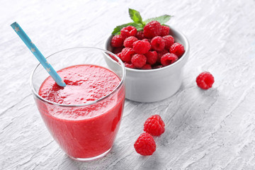 Glass of tasty raspberry smoothie and bowl with fresh berries on table