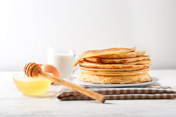 Bowl of honey and plate with stack of tasty thin pancakes on table