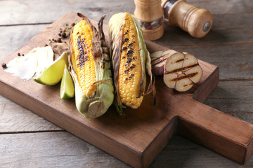 Wooden board with delicious grilled corn on table