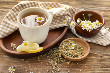 Bowls with camomile and delicious tea on wooden table