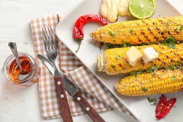Plate with tasty grilled corn cobs on table