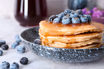 Bowl with tasty pancakes and blueberries on light table, closeup