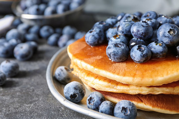 Plate with tasty pancakes and blueberries on dark table, closeup