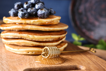 Tasty pancakes with blueberries and honey dipper on board, closeup