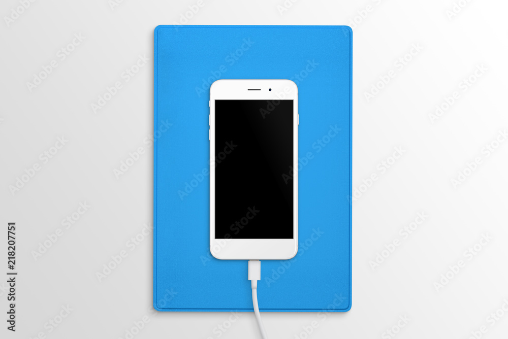 Poster phone connected to the charger on desk. blue folder in background. top view. blank screen for mockup