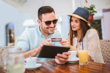 Surprised young couple doing online shopping through digital tablet and credit card at cafe.