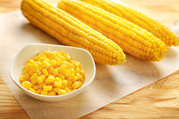 Bowl with corn kernels and cobs on wooden table, closeup