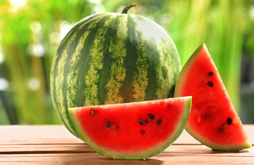 Delicious watermelon and slices on wooden table against blurred background