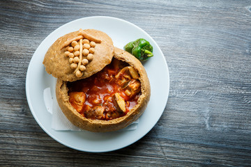 fish soup in original homemade brown bread bowl on white plate with green pepper