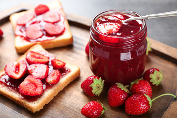 Glass jar with delicious strawberry jam and slices of bread on board, closeup