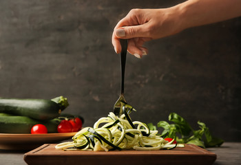 Woman holding fork with zucchini noodles over wooden board in kitchen