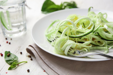 Plate with zucchini spaghetti on table, closeup