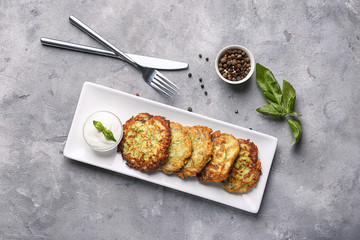 Plate with zucchini pancakes and sauce on table