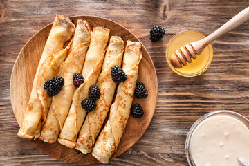 Plate with tasty thin pancakes, berries, sour cream and honey on wooden table