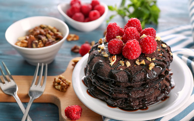 Plate with tasty chocolate pancakes and berries on board