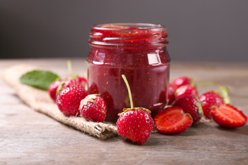Glass jar with delicious strawberry jam on wooden table