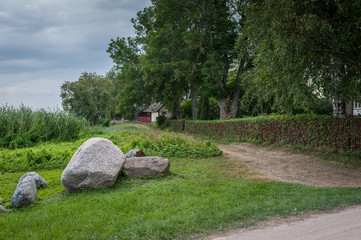 Landscape in the countryside. Typical view with dirt road, stones and in the background a white wooden house with fence. Estonia.