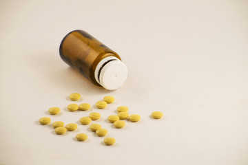 Medicine bottle of brown glass with pills and tablets. Pills from bottle on the white background. Yellow pills in a bottle.