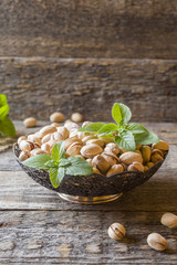 Delicious salted pistachios and fresh mint leaves on wooden background.