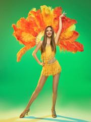 young beautiful dancer with carnival feather and fringe posing on studio background