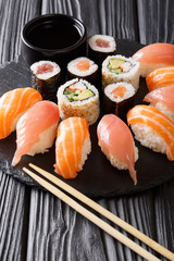 The Japanese menu. Tasty set of sushi with salmon and tuna, California rolls, maki, soy sauce closeup on a black slate board on the table. vertical