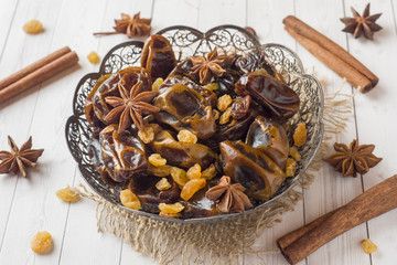 Oriental sweets, dried fruit dates and raisins, cinnamon and star anise in a plate. Turkish tea in glasses on a wooden background.