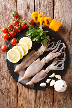 Raw fresh squid close-up and vegetable for cooking on a slate board. Vertical top view from above
