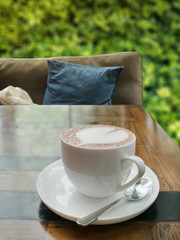 close up of a cup of hot chocolate with heart on wood table and comfortable sofa,blur tree background