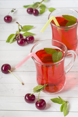 Cherry juice with mint leaves and fresh cherries on a white wooden table.