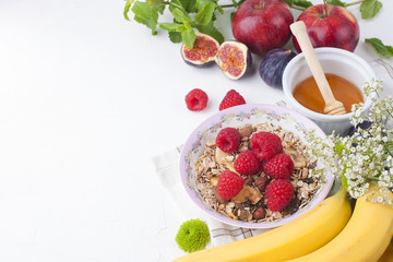 Delicious and healthy breakfast on a white background. Porridge of oatmeal, raspberry, honey, bananas, figs, mint fresh for a good morning. Free space for text, top view