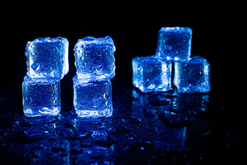 Blue ice cubes reflection on black table background.