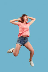 Freedom in moving. Mid-air shot of pretty happy young woman jumping and gesturing against blue studio background. Runnin girl in motion or movement. Human emotions and facial expressions concept