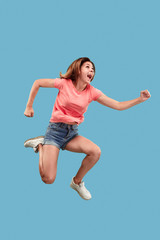 Freedom in moving. Mid-air shot of pretty happy young woman jumping and gesturing against blue...