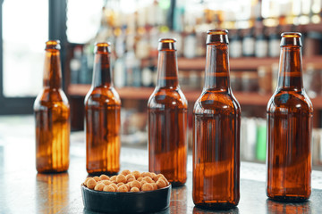 Brown glass beer bottles with small bowl of salty nuts arranged on top of counter in modern bar