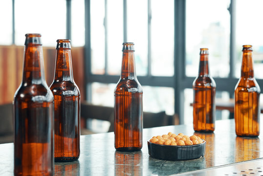 Bar counter with bowl of salty snack and brown glass beer bottles in daylight