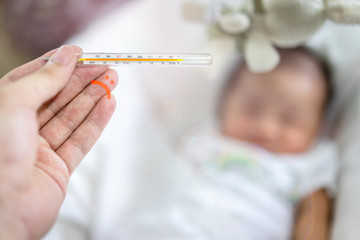 Hand holding a thermometer with high temperature on blur crying baby background.