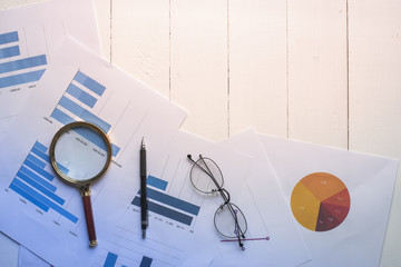 Magnifying glass and documents with analytics data lying on table,selective focus