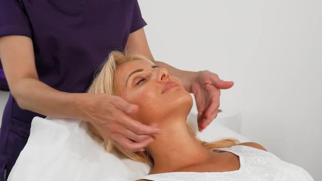 Cropped shot of a happy mature woman smiling with her eyes closed while professional beautician massaging her neck. Attractive woman getting facial treatment by cosmetologist.