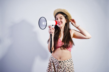 Portrait of a gorgeous young girl in swimming suit and hat talks into megaphone in studio.