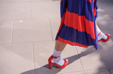 Young woman wearing stylish red skirt and shoes on an urban sidewalk. Low angle view of her shapely legs. Selective focus