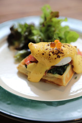 Breakfast food egg benedict , poached egg with yellow sauce with waffle and smoked salmon on wood background