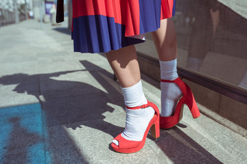 Young woman wearing stylish red skirt and shoes on an urban sidewalk. Low angle view of her shapely legs. Selective focus