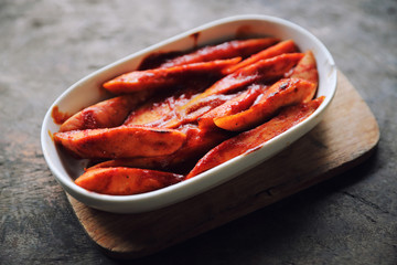 Traditional German currywurst pieces of sausage with curry sauce on wood background