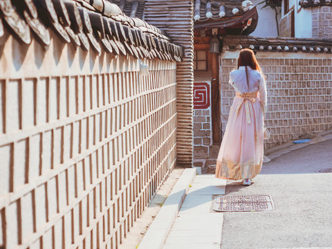 travel and tourist asia concept from backside long hair woman in korea traditional cloth (hanbok) walk in vintage town and old brick wall with soft focus background