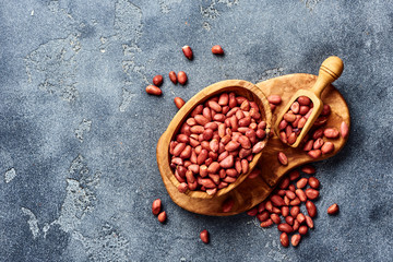 Peeled peanuts in bowl and scoop on gray background. Top view of nuts.