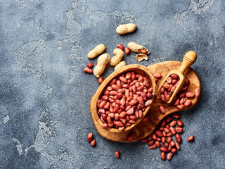 Peeled peanuts in bowl and scoop on gray background. Top view of nuts.