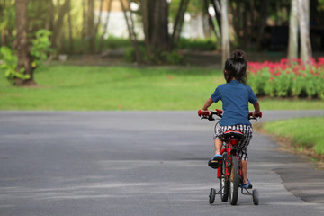 Back of Asian girl riding the bicycle sport kids happiness on the road in public park of Thailand