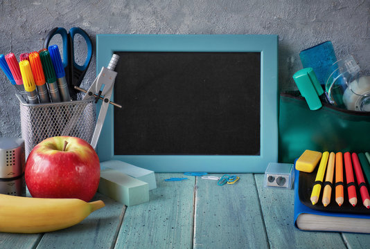 Stationery and fruits on a table in front of blackboard with text space
